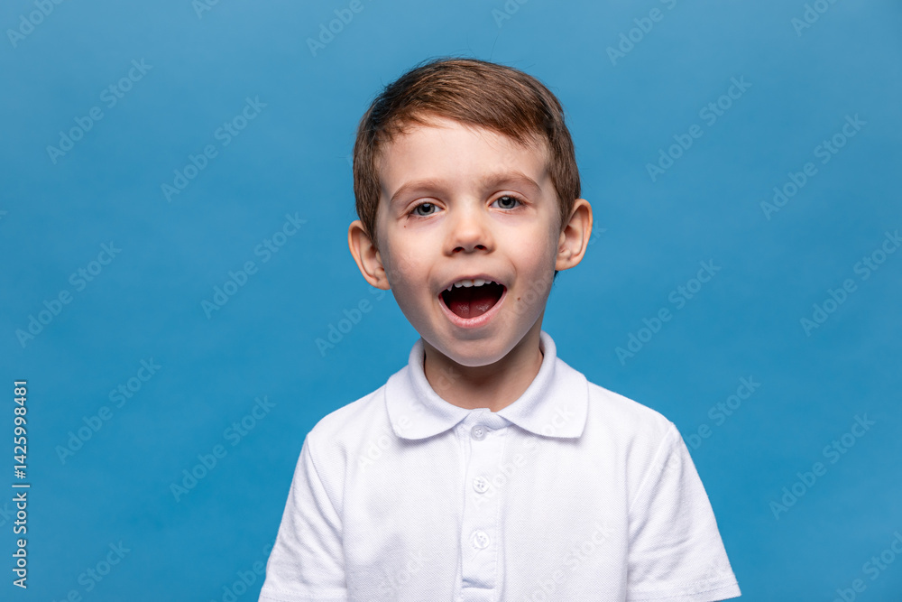 Portrait of scared little boy wearing white t-shirt making a grimace with his mouth open and hands up. Child is very surprised on white background. Mock up. Shock, amazement, surprise concept.