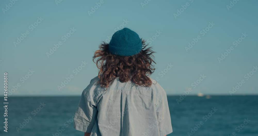 custom made wallpaper toronto digitalAuthentic young woman in blue themed outfit, striped t-shirt, hand knitted blue wool beanie and prescription glasses and curly hair looks at ocean and then directly at camera. Candid image of youth