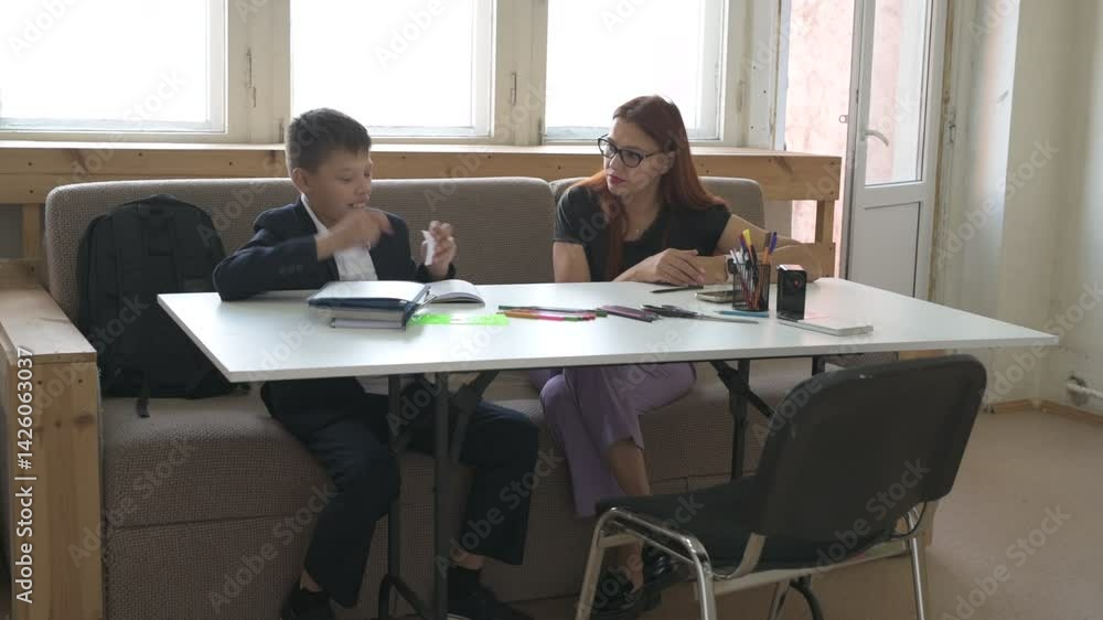 A homeschooled schoolboy does his homework with mom at desk. boy studies with a tutor at home A homeschooled schoolboy does his homework with mom at desk. boy studies with a tutor at home