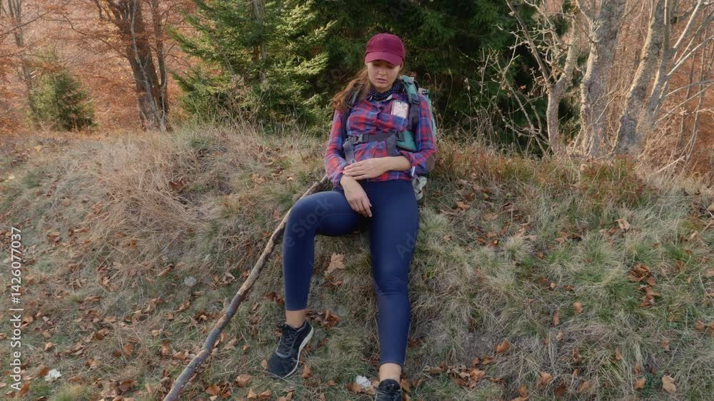 Full-body shot of a tired young woman resting on a grassy forest hillside after a challenging hike. Great for outdoor adventure, fatigue, perseverance, and solo travel concept footage. Full-body shot of a tired young woman resting on a grassy forest hillside after a challenging hike. Great for outdoor adventure, fatigue, perseverance, and solo travel concept footage.