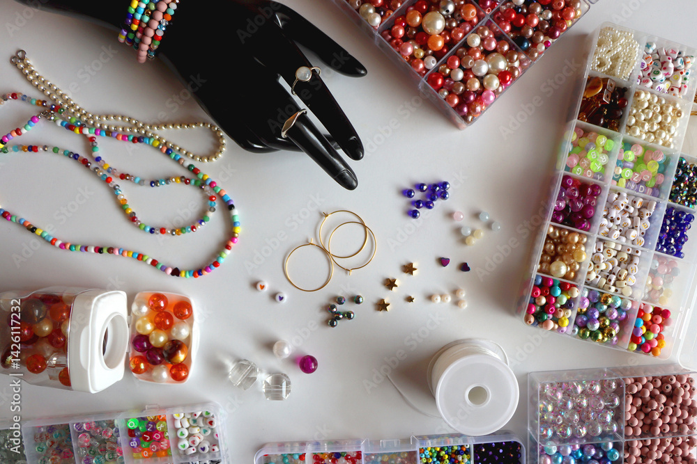 Hand figurine, colorful friendship bracelets, necklaces, various beads and DIY supplies on the table. Making jewelry at home. Flat lay.