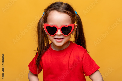 Obraz na płótnie Smiling little child girl dressed in a red t-shirt and red funny sunglasses on yellow studio background. Summer travel vacation with children, advertising concept. Banner, mock up, copy space w salonie