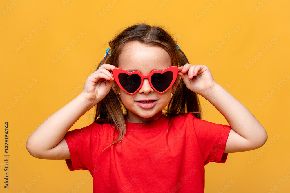 Smiling little child girl dressed in a red t-shirt and red funny sunglasses on yellow studio background. Summer travel vacation with children, advertising concept. Banner, mock up, copy space