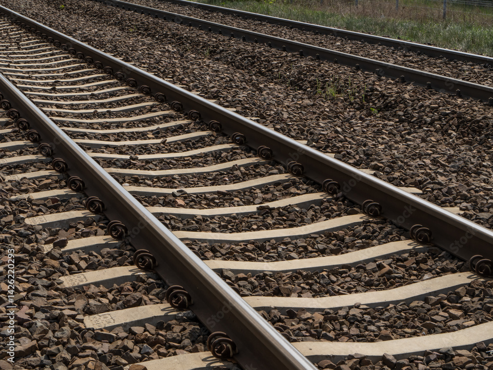 Naklejka premium Close-up view of railway tracks with concrete sleepers and ballast gravel, showing the rhythmic structure and alignment of train infrastructure.
