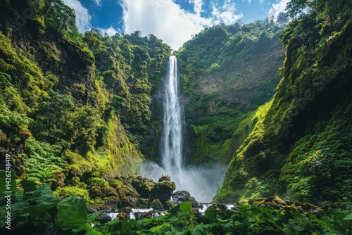 Majestic waterfall cascading down cliffs surrounded by lush green vegetation and bright blue sky