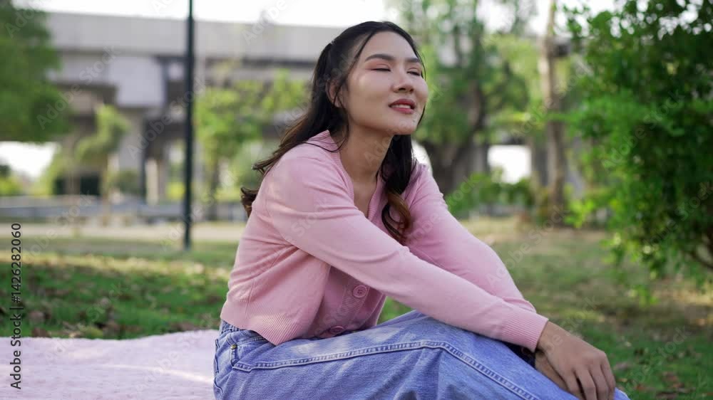 Locked medium shot, Young Asian woman sitting on grass sward while relaxation in park, She smile with happy at beautiful park Locked medium shot, Young Asian woman sitting on grass sward while relaxation in park, She smile with happy at beautiful park
