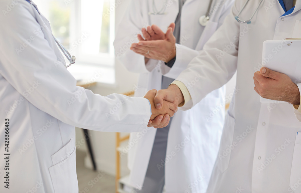 Close up cropped view of two professional doctors in white lab coats shaking hands in clinic. Medical staff exchanging handshake and applauding, celebrating teamwork or success in patient treatment.