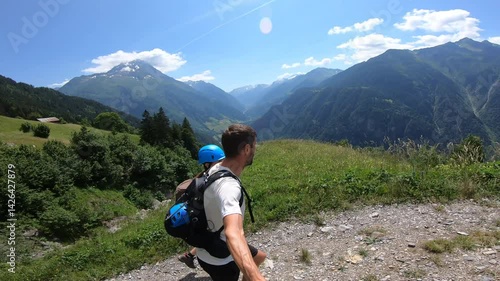 Two hikers walk on a grassy ridge, admiring panoramic alpine views and the vast mountain scenery surrounding the Hexensteig via ferrata.