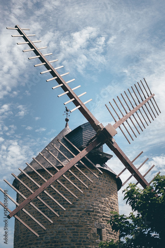 Old stone windmill with wooden blades captured on a sunny day with scattered clouds. Charming countryside architecture and rural atmosphere