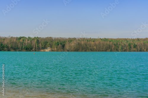 Bright turquoise lake surrounded by forest under clear sky