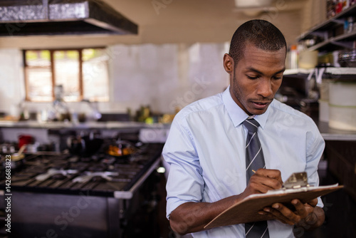 фотографія Mid-adult African American man using clipboard in commercial kitchen, with gas r
