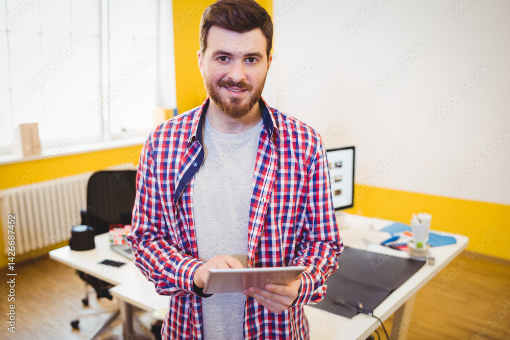 Male office worker holding tablet in modern office, with computer monitor, mouse pad and coffee cup