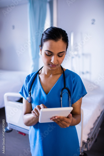 Obraz na płótnie Young Indian nurse standing in hospital room, checking tablet with stethoscope and IV stand w salonie