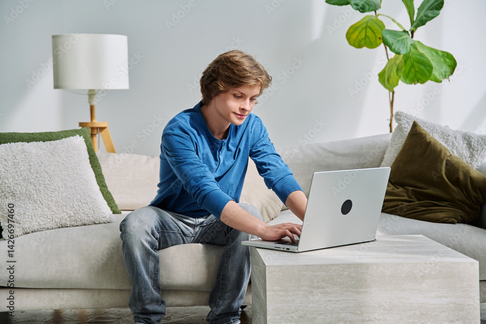Handsome smiling teenage boy sitting at home on the couch typing on laptop