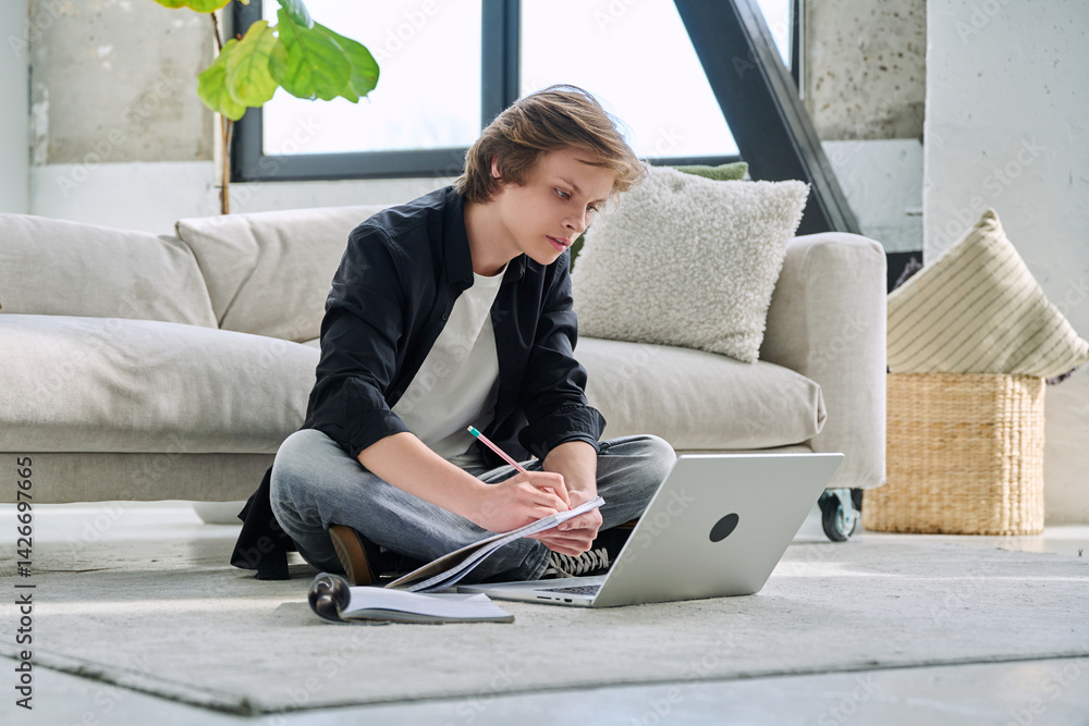 Teenager guy student studying sitting at home on the floor using laptop textbook notebook
