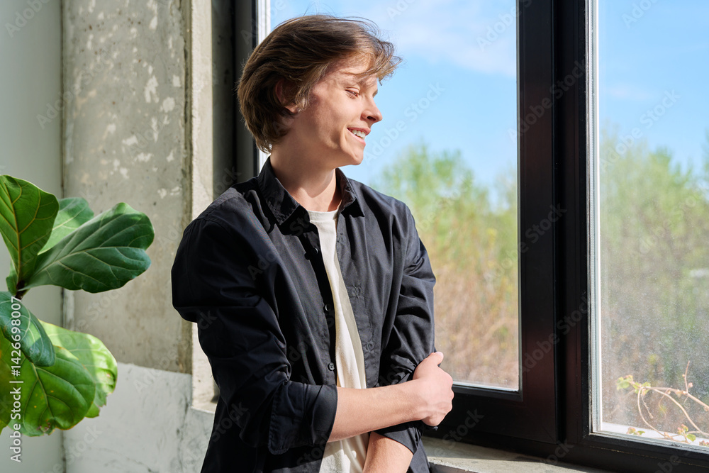Handsome young smiling guy looking out the window