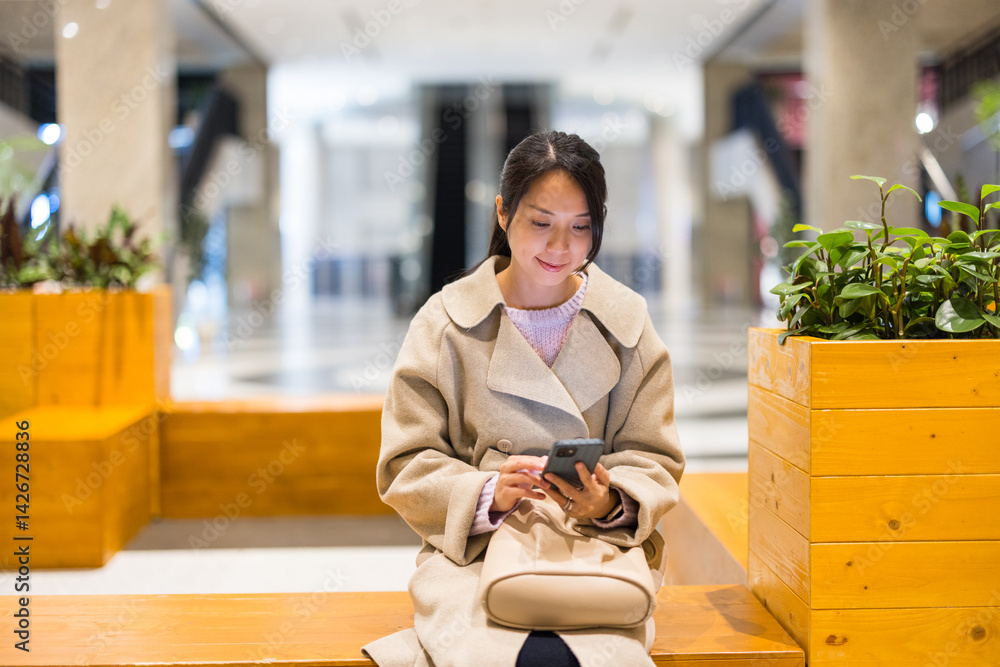 Businesswoman sitting in shopping centre using mobile phone