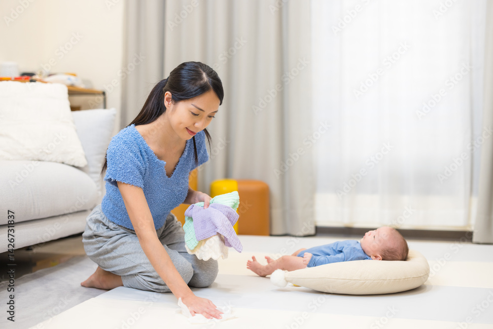 Mum tidying playpen with baby at home in morning