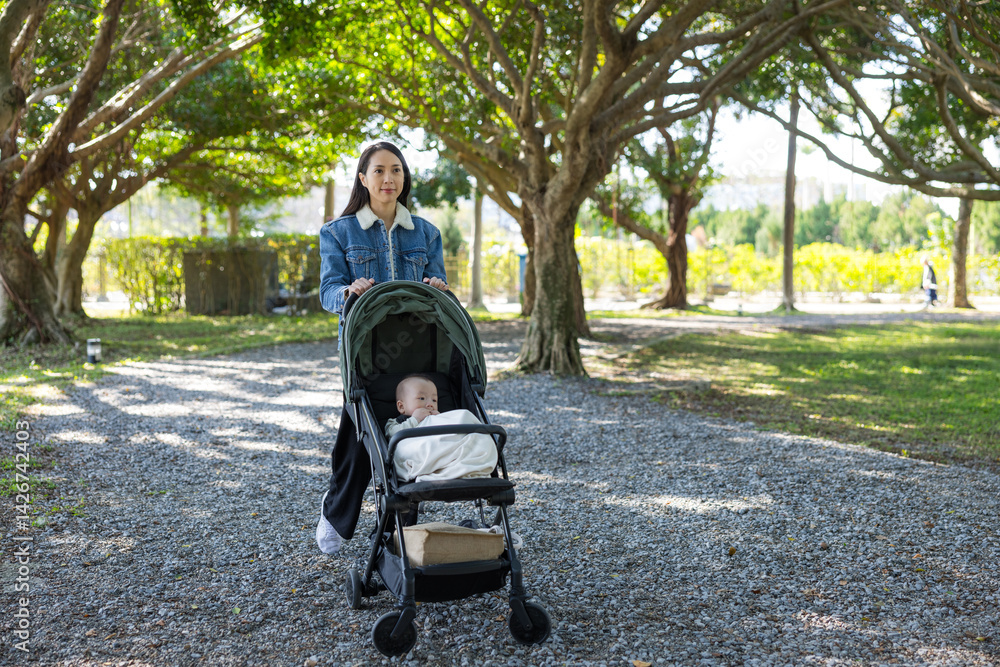 Mother pushing baby stroller in green park