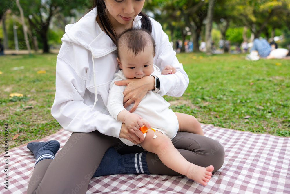 Mum applying sunblock lotion on her baby son at park
