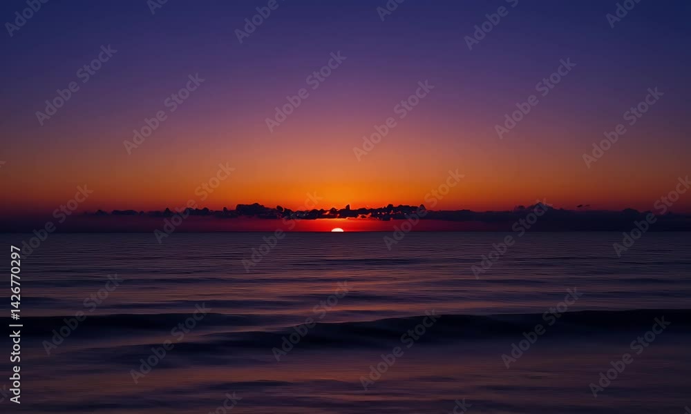 Ocean sunset with brilliant oranges & purples. Gentle waves reflect sun. Clouds hug horizon Ocean sunset with brilliant oranges & purples. Gentle waves reflect sun. Clouds hug horizon