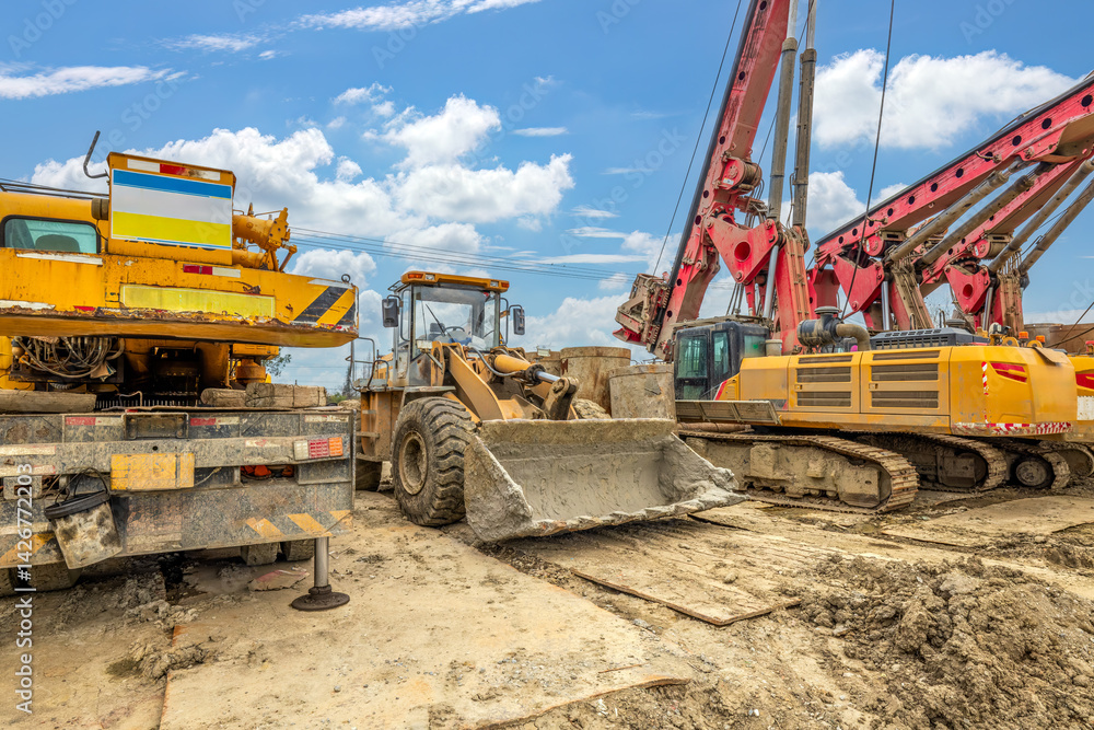 Heavy construction machinery including yellow loader and red drilling rig at outdoor site. Heavy construction machinery including yellow loader and red drilling rig at outdoor site.