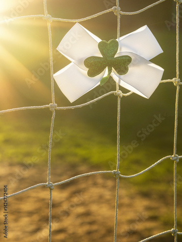 Obraz na płótnie White bow with green Irish shamrock attached on a goal post net. Support for national sport of Ireland, hurling, Gaelic football, rugby, camogie. Selective focus. Boys in green fan base. Sun flare. w salonie