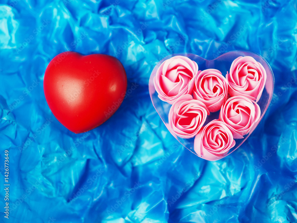 A heart made of pink roses is placed on a blue background and red heart. The roses are arranged in a way that they look like they are floating in the air. Concept of love and romance