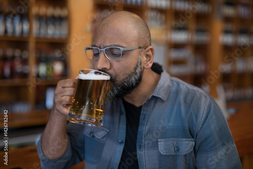 Wallpaper Mural Indian man sipping beer from large glass mug at wooden bar counter, surrounded by bottled beers Torontodigital.ca