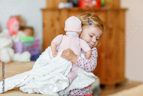 Obraz na płótnie Adorable cute little toddler girl playing with doll. Happy healthy baby child having fun with role game, playing mother at home or nursery. Active daughter with toy. w salonie