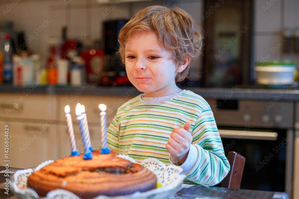 Adorable four year old boy celebrating his birthday and blowing off the candles on the cake, indoor. Happy child with big cake.