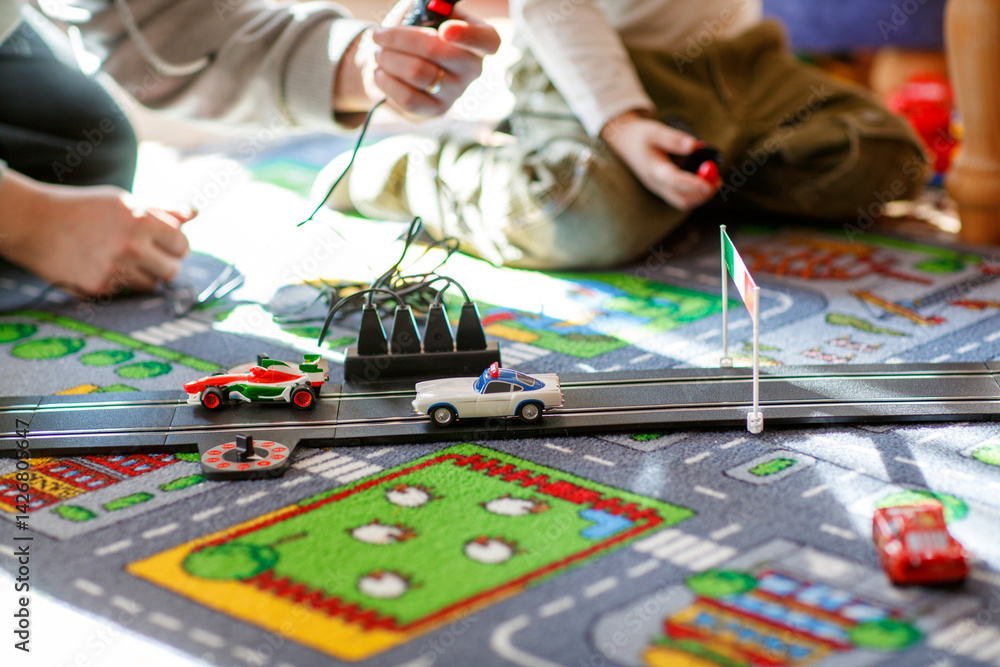 Father and son playing with racing cars on racetrack, indoors, with cars. Happy little preschool boy and young man having fun with indoor race game