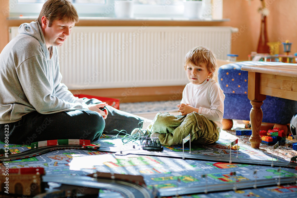 Father and son playing with racing cars on racetrack, indoors, with cars. Happy little preschool boy and young man having fun with indoor race game