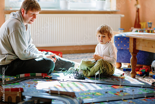 Obraz na płótnie Father and son playing with racing cars on racetrack, indoors, with cars. Happy little preschool boy and young man having fun with indoor race game w salonie