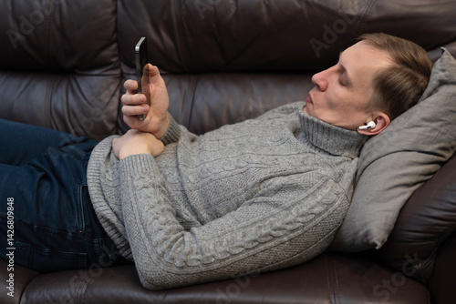 Relaxed man using a smartphone lying down on the couch in the living room at home