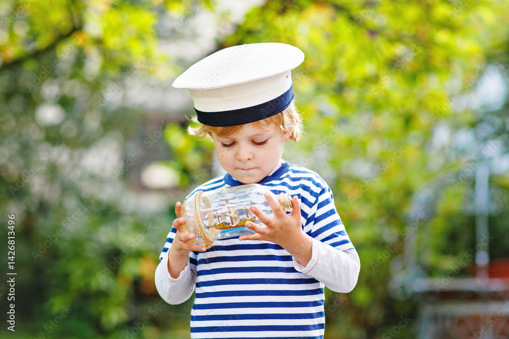 Happy little kid boy in sailor capitain hat and uniform playing with sailor boat ship. Smiling preschool child dreaming and having fun. Education, profession, dream concept