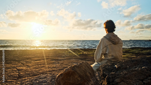 Man on a beach is looking distance during beautiful summer sunset. Human looks to the sun over horizon in the morning while sunrise. Happy person contemplates the beauty of nature. Freedom concept.