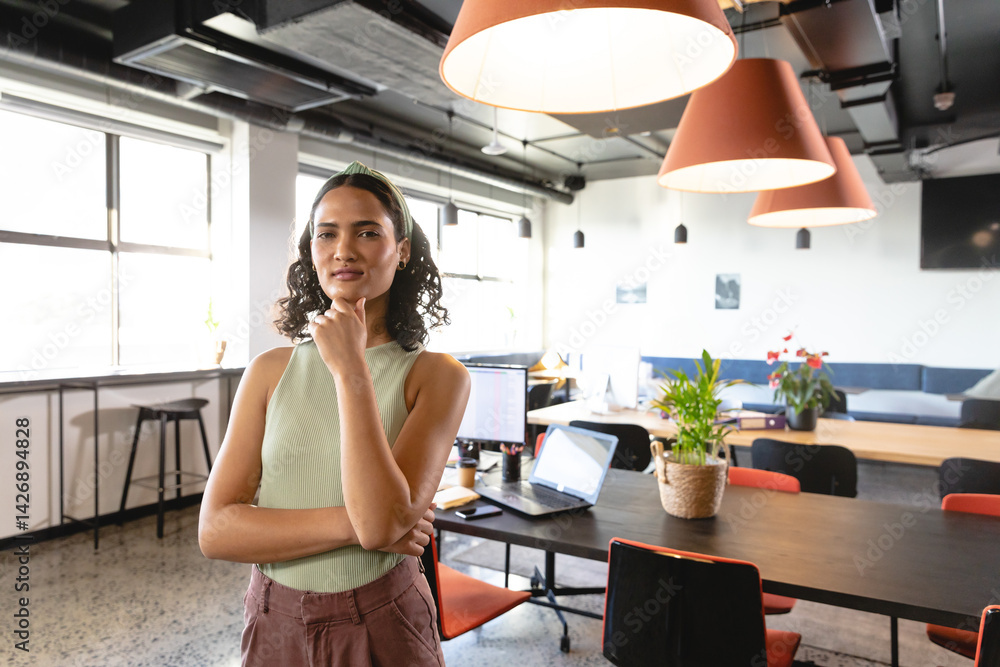 Professional woman standing confidently in modern open-plan office, with laptops and plants Professional woman standing confidently in modern open-plan office, with laptops and plants