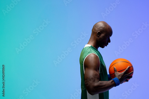 African American man holding basketball with green-white jersey against studio backdrop, copy space