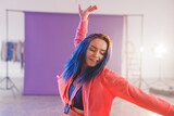 Non-binary young adult dancing in photography studio with purple backdrop and action camera harness