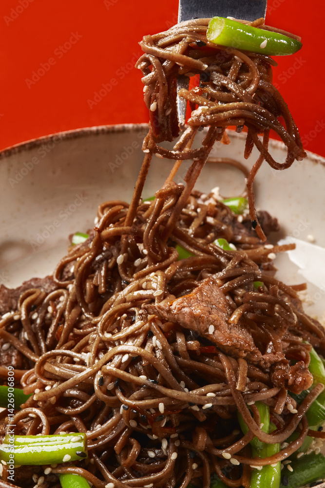 Fork lifting soba noodles with beef and green beans from bowl
