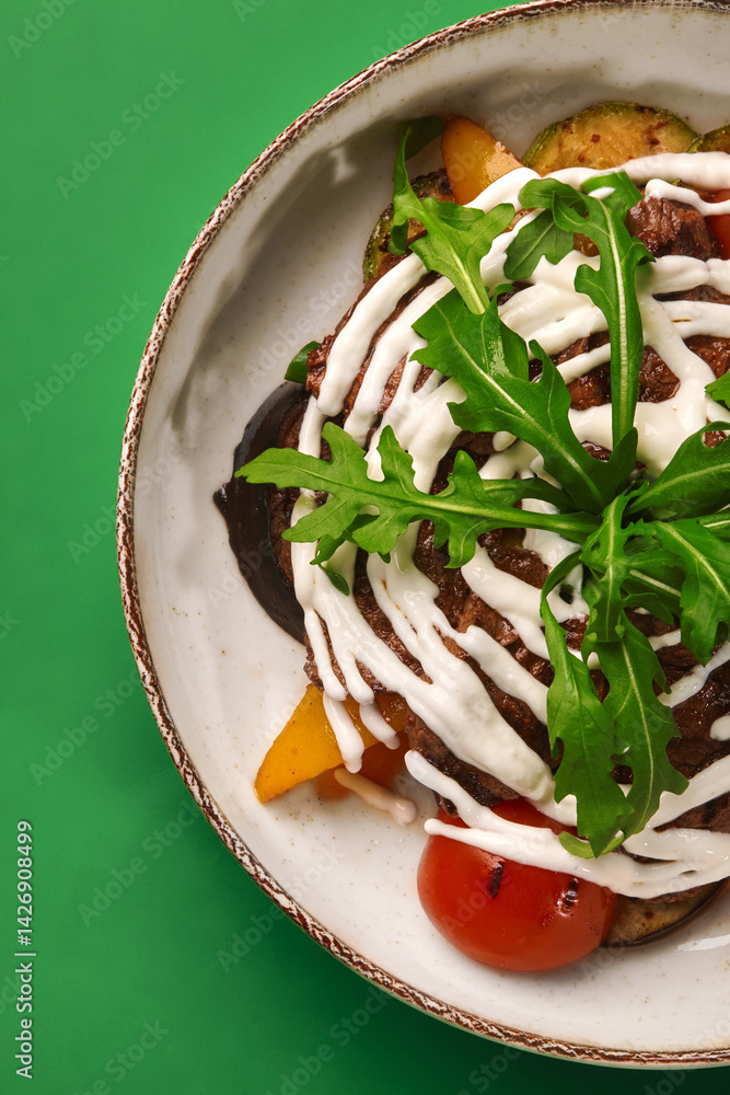 Grilled beef steak with vegetables and yogurt sauce on green background