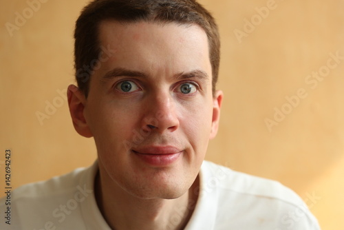 Young man face with dark hair on a light brown background.