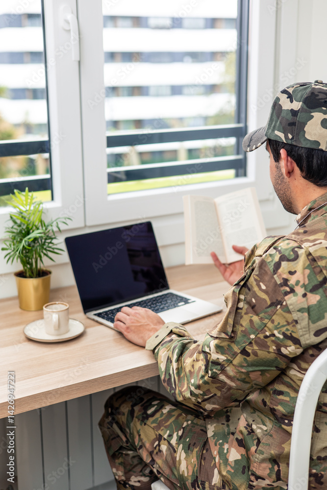 Fototapeta premium vertical Soldier studying using laptop and book at home