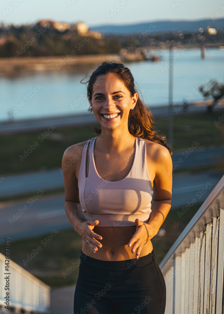 Smiling Woman Jogging Outdoors Near a Scenic Riverside During Sunset