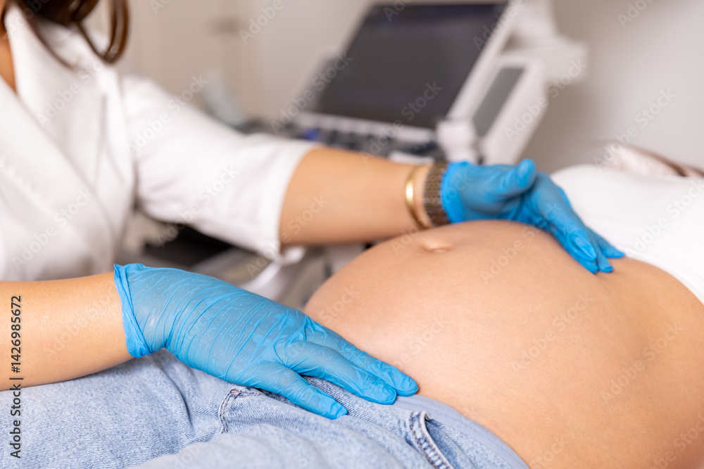 Close up shot of female doctor in medical gloves examining pregnant woman lying on bed in clinic. Palpation of womb belly, feeling baby fetus embryo bumps. Gynecologist check up. High quality photo