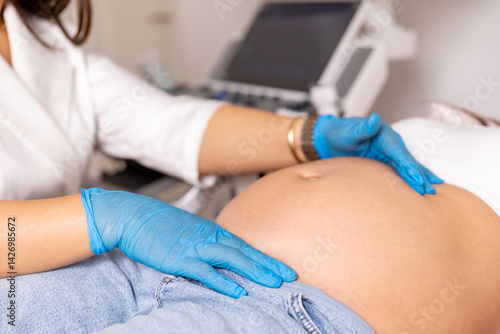 Obraz na płótnie Close up shot of female doctor in medical gloves examining pregnant woman lying on bed in clinic. Palpation of womb belly, feeling baby fetus embryo bumps. Gynecologist check up. High quality photo w salonie