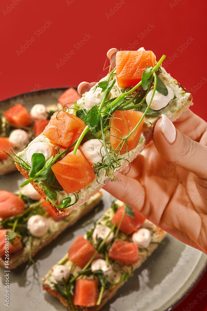 Woman holding a salmon toast with cream cheese and microgreens over a plate of toasts