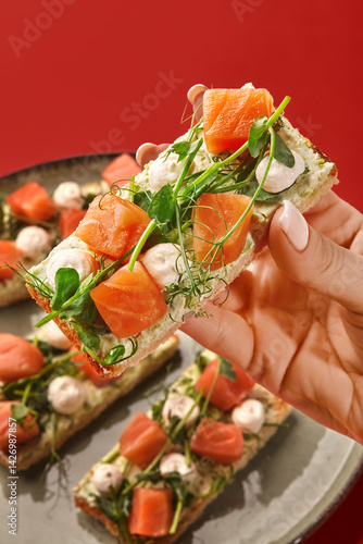 Obraz na płótnie Woman holding a salmon toast with cream cheese and microgreens over a plate of toasts w salonie