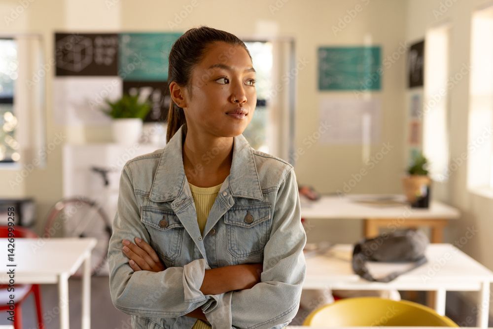 Asian Chinese woman standing with arms crossed and looking right in classroom with bicycle backpack Asian Chinese woman standing with arms crossed and looking right in classroom with bicycle backpack